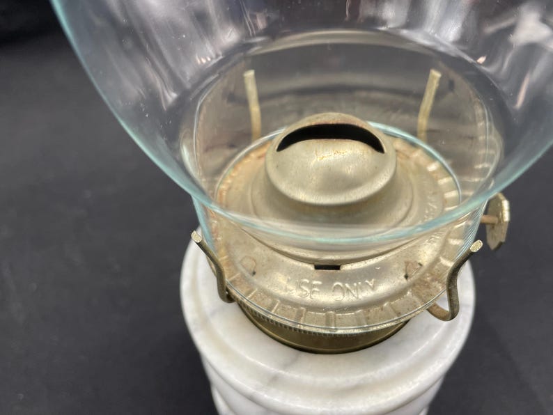 May include: Close-up of an antique oil lamp. The lamp features a clear glass globe, a brass burner assembly, and a white marble base. The burner is marked "USE ONLY".