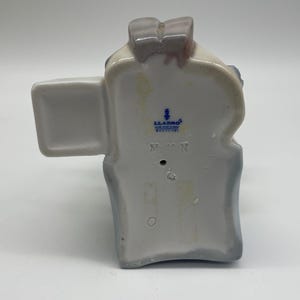 May include: A white porcelain figurine of a woman wearing a blue dress and a white hat. The figurine is holding a bouquet of flowers. The figurine is marked with the Lladro logo and the number 5710.