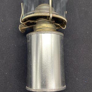 May include: A vintage oil lamp with a clear glass globe and a silver metal base. The lamp has a brass-colored burner assembly and a metal handle for carrying. The lamp is designed for use with oil and provides a classic lighting solution.