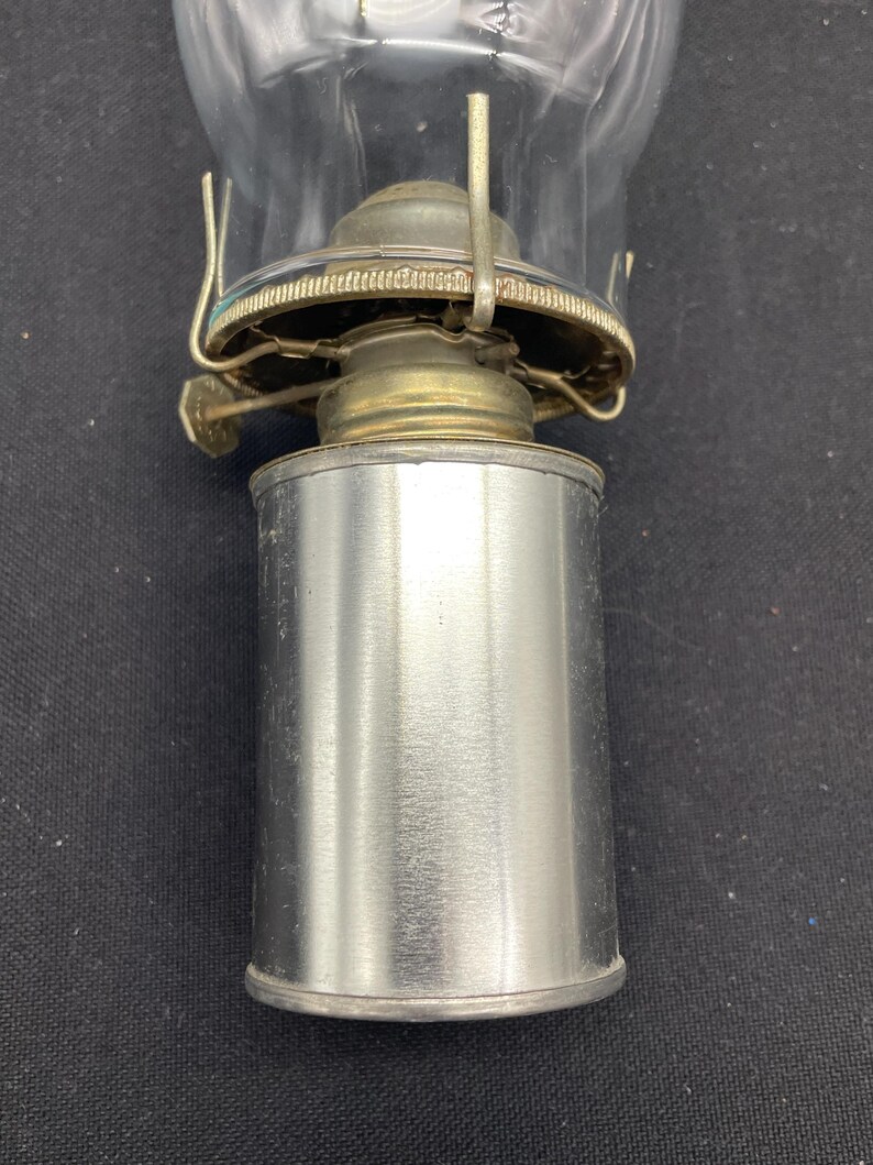 May include: A vintage oil lamp with a clear glass globe and a silver metal base. The lamp has a brass-colored burner assembly and a metal handle for carrying. The lamp is designed for use with oil and provides a classic lighting solution.