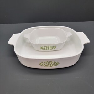 May include: A white ceramic baking dish with a green floral design. The dish is nested inside a larger white ceramic baking dish with the same design.