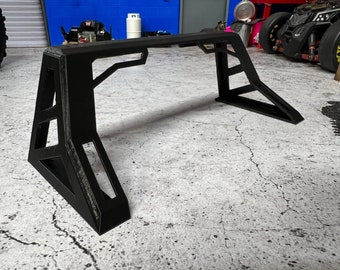 Pode incluir: Suporte de metal preto com um design geométrico. O suporte é feito de metal resistente e tem um acabamento preto. É projetado para segurar objetos com segurança.