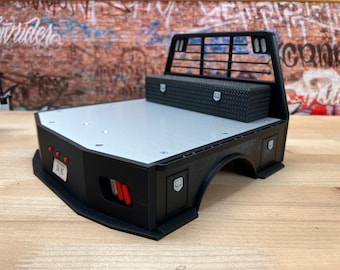 May include: Black truck bed with a white bed liner, a black toolbox, and a black metal bed rack. The truck bed has red taillights and a license plate that says "3K".