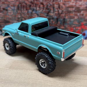 Peut inclure: Un camion jouet de couleur turquoise avec de gros pneus tout-terrain noirs. Le camion a une benne noire et des garnitures chromées. Le modèle est une réplique miniature d'un pick-up classique.