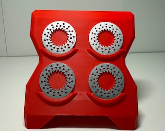 May include: A red, 3D-printed holder with four circular, silver-colored metal discs. Each disc has a series of small holes around the perimeter. The holder has a unique, geometric shape with a wide base and a curved top.
