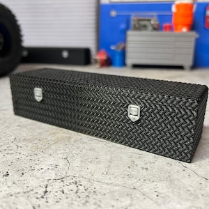 May include: Black metal toolbox with diamond plate pattern and two latches. The toolbox is sitting on a gray concrete surface.