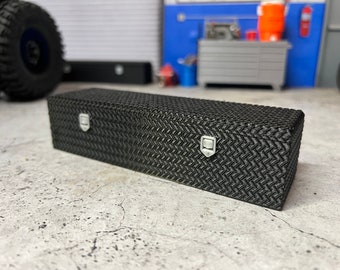 May include: Black metal toolbox with diamond plate pattern and two latches. The toolbox is sitting on a gray concrete surface.