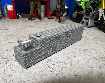 Pode incluir: Um tanque de combustível de metal prateado com um padrão de placa de diamante. O tanque tem uma tampa na parte superior e um bico lateral.