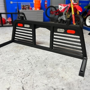 May include: Black metal truck bed rack with a slatted design and two red lights on the back.