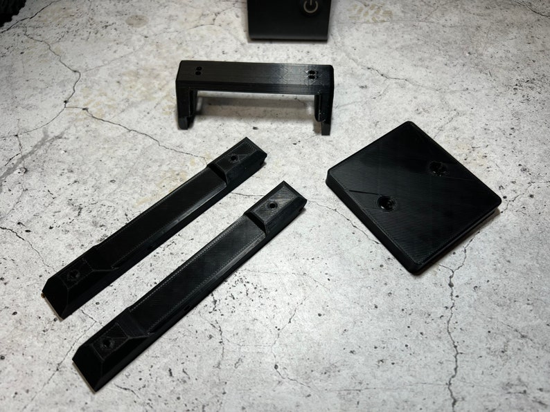 May include: A set of four black plastic 3D printed parts for a DIY project. The parts include two long rectangular pieces, a short rectangular piece, and a square piece.