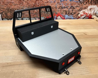 May include: Black and silver model truck bed with a diamond-patterned toolbox. The bed has a silver surface and a black frame with a rear rack. Includes red taillights and a license plate that reads "SB RC".