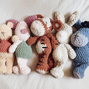 Op de afbeelding: Vijf gehaakte knuffeldieren op een rij. De collectie bestaat uit een crème en roestkleurige beer, een roze en saliegroen konijn, een bruin met wit gestreepte tijger, een crème konijn met lange oren en een blauwe ezel met zwarte manen.