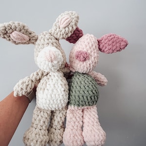 May include: Two handmade crochet plush toys. One is a beige rabbit with a white belly and pink inner ears. The other is a pig with a light pink head, dark pink ears and snout, and a sage green body. Both are crafted from soft, chunky yarn.