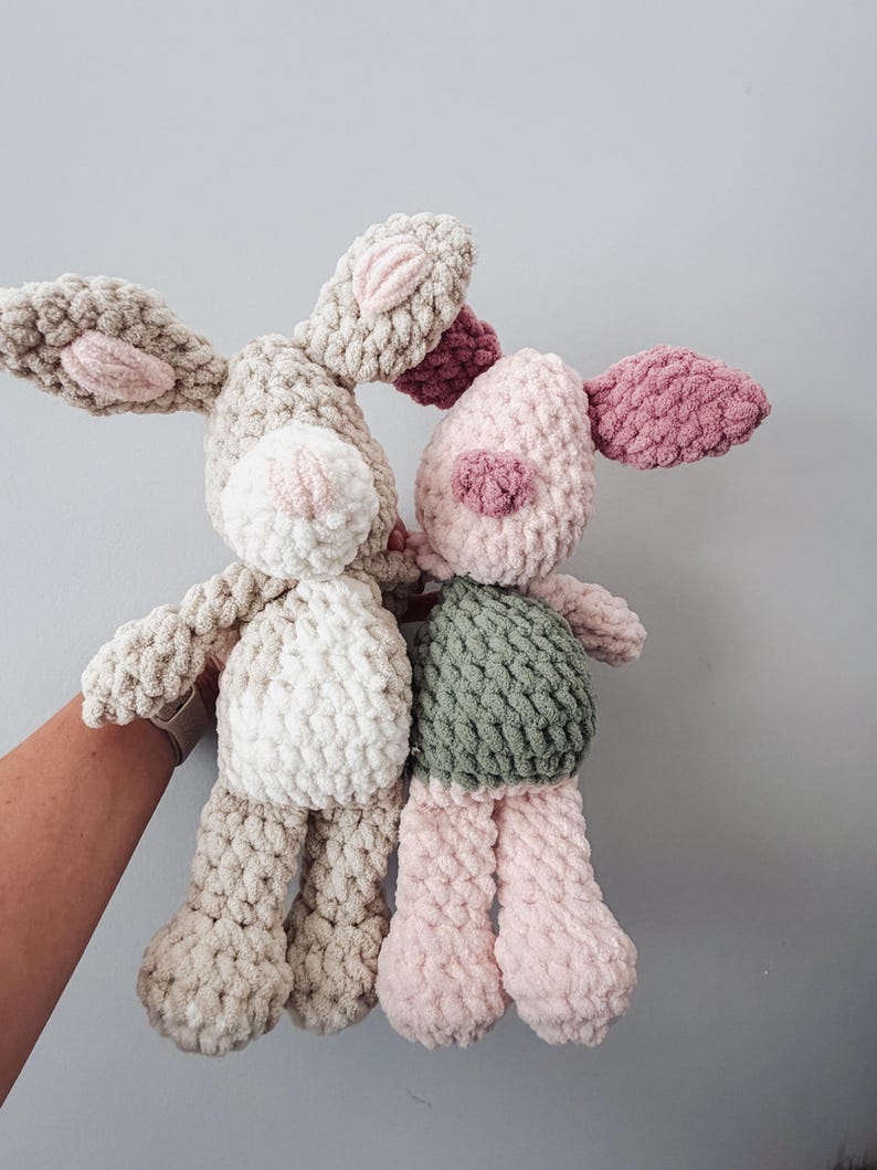 May include: Two handmade crochet plush toys. One is a beige rabbit with a white belly and pink inner ears. The other is a pig with a light pink head, dark pink ears and snout, and a sage green body. Both are crafted from soft, chunky yarn.