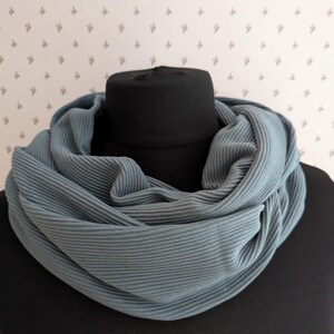 Könnte beinhalten: Ein weicher, gerippter, blau-grauer Loop-Schal liegt über einem schwarzen Mannequinkopf. Der Schal besteht aus einem leichten Material und ist zum Tragen um den Hals konzipiert. Der Stoff hat einen dezenten Glanz.