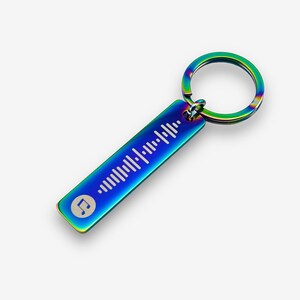 May include: A rainbow-colored metal keychain with a music note and a barcode design. The keychain is attached to a silver ring.