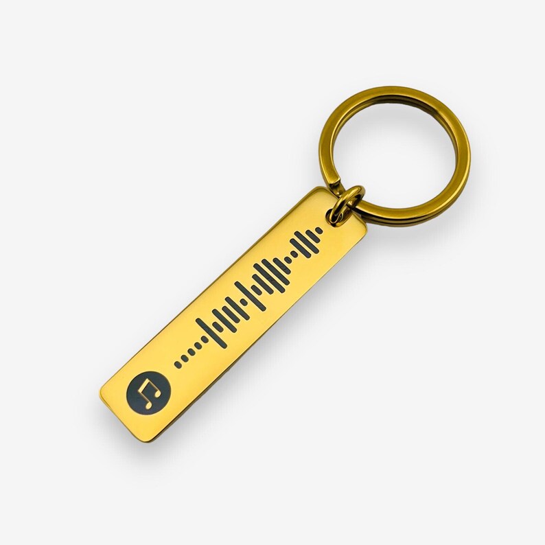 May include: Gold-colored metal keychain with a black musical note and a black and white sound wave pattern.