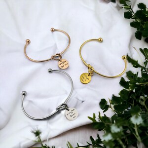 Puede incluir: Tres pulseras de nudo de oro con un dije redondo adjunto a cada una. Los dijes tienen mensajes escritos a mano: "lots of love Dad xxx", "I love you more than C", y "always love you more".