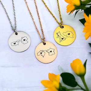 Puede incluir: Tres collares de plata, oro y oro rosa con colgantes redondos que representan los contornos de dos continentes con corazones en el centro. Los continentes están conectados por una línea punteada.