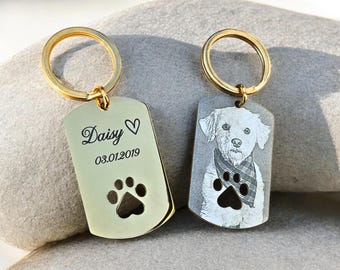 May include: Two personalised dog tag keyrings. One gold-coloured tag features the name "Daisy", a heart, the date 03.01.2019, and a paw print cutout. The other tag displays a dog portrait and paw print.