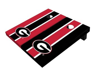 May include: A set of two red and black cornhole boards with a white stripe design and a large black and white "G" logo on each board.