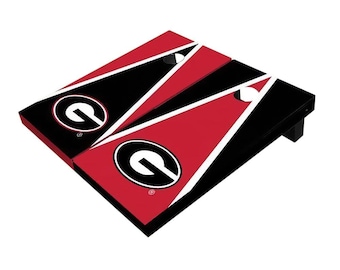 May include: A cornhole game set featuring two boards with a red, black, and white design. Each board has a large "G" logo in a black circle. White bean bags are visible on the boards.