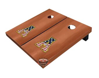 May include: A pair of wooden cornhole boards with a brown finish. Each board features a large letter "A" in red, white, and blue, resembling the American flag. The boards have a hole near the top and are supported by black legs.