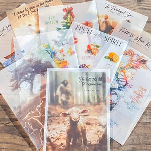 May include: A collection of translucent vellum sheets featuring various religious illustrations and scripture verses, including text such as He left the 99 to rescue me, Fruit of the Spirit, The Prodigal Son, and I praise you because I am fearfully and wonderfully made.