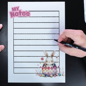 May include: A lined notepad with the text "MY Notes" and a watercolor illustration of an Easter bunny inside an egg. A person is writing on the notepad with a black pen. A white computer mouse and a vase with white flowers are also visible.