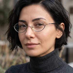 May include: Oval-shaped spectacles with thin, dark metal frames and clear lenses. The glasses feature a bridge that connects the two rims at the top, creating a distinct silhouette. The frames are lightweight and have adjustable nose pads.