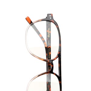 May include: Tortoiseshell eyeglasses with a brown and black mottled pattern. The inner temple arm features the text Vita Vintage made in Khalkedon. The frames have a rounded shape with a bridge connecting the upper portion of the lenses.