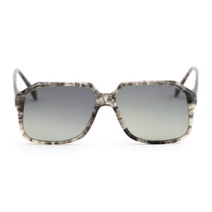 May include: Square-framed sunglasses with a marbled gray and white pattern. The lenses are a gradient gray, transitioning from dark at the top to lighter at the bottom. The frames have a thick, angular design, and the temples are thin and dark.