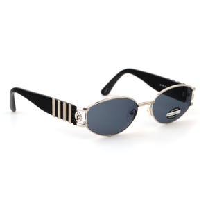 May include: Oval-shaped sunglasses with a silver frame and dark blue lenses. The temples are black with silver stripes and a logo. The sunglasses have a classic, retro design.