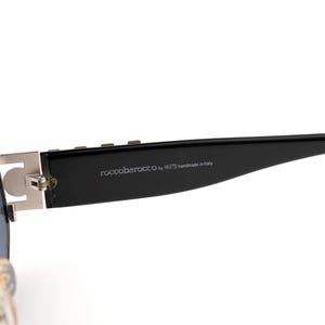 May include: Close-up of a pair of sunglasses. The sunglasses have a black frame with silver accents and the text "roccobarocco by handmade in Italy" printed on the arm.