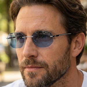 May include: Rimless sunglasses featuring light blue gradient lenses and thin silver metal temples. The glasses have a sleek, minimalist design with a bridge connecting the two lenses and slender arms that extend along the sides of the face.