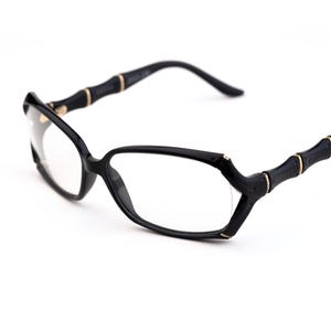 May include: Black eyeglasses with a unique bamboo-style design on the temples. The frames are black with gold-colored accents. The lenses are clear. The glasses have a modern, stylish look.