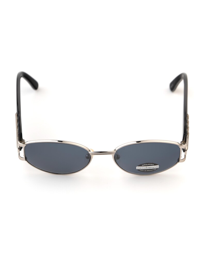 May include: Oval-shaped sunglasses with a silver frame and dark gray lenses. The temples are black and feature a decorative design. The sunglasses have a small sticker on the lens.