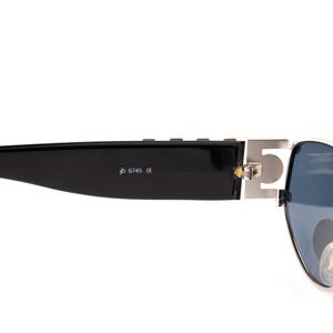 May include: Black sunglasses with a silver metal accent on the temple. The sunglasses have dark blue lenses and the text "6745 CE" is printed on the black arm.