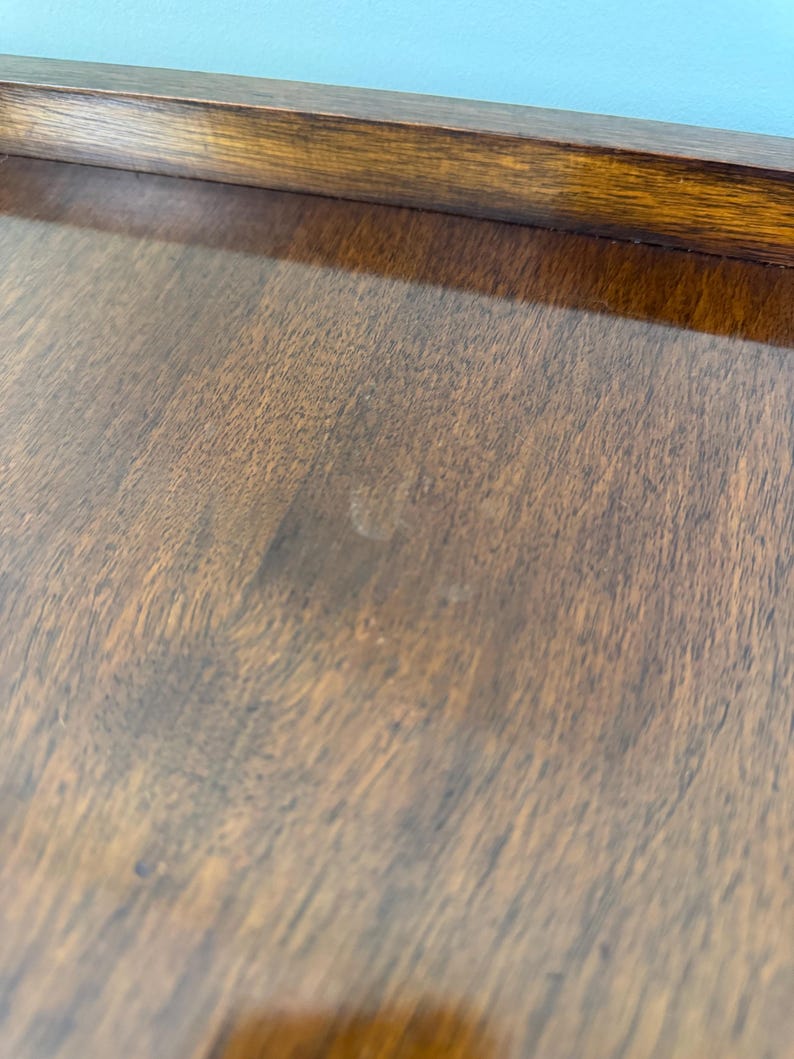 May include: Close-up of a wooden surface with a rich, dark brown colour and visible wood grain. The surface has a smooth, polished appearance, with a darker brown border at the top. The wood appears to be well-maintained.