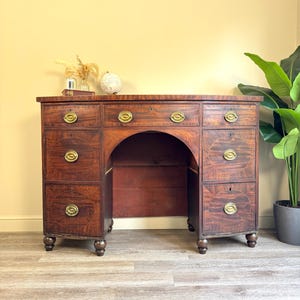 May include: A dark wood desk with multiple drawers and a central arched space. The desk has brass handles and is a classic piece of furniture. The desk is a vintage item, ideal for a home office or study. The desk's dimensions are approximately 150 cm wide.