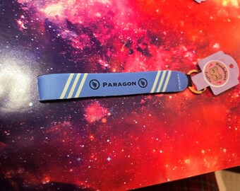 May include: A blue and white striped key chain with the word "PARAGON" printed in black. The key chain has a small silver ring attached to it.