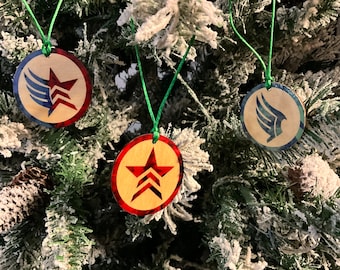 Könnte beinhalten: Drei runde Weihnachtsbaumkugeln aus Holz mit einem roten, weißen und blauen Stern- und Flügeldesign. Die Kugeln hängen an einem grünen Weihnachtsbaum.