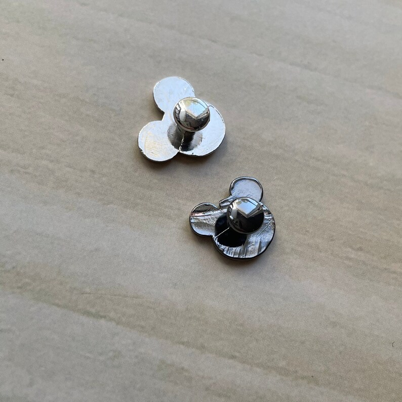 May include: Two silver metal Mickey Mouse head pins with a pin back.
