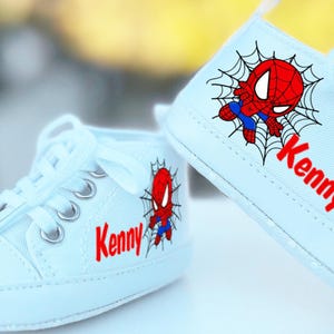 May include: A pair of light blue baby shoes with a Spiderman design and the name "Kenny" on each shoe.