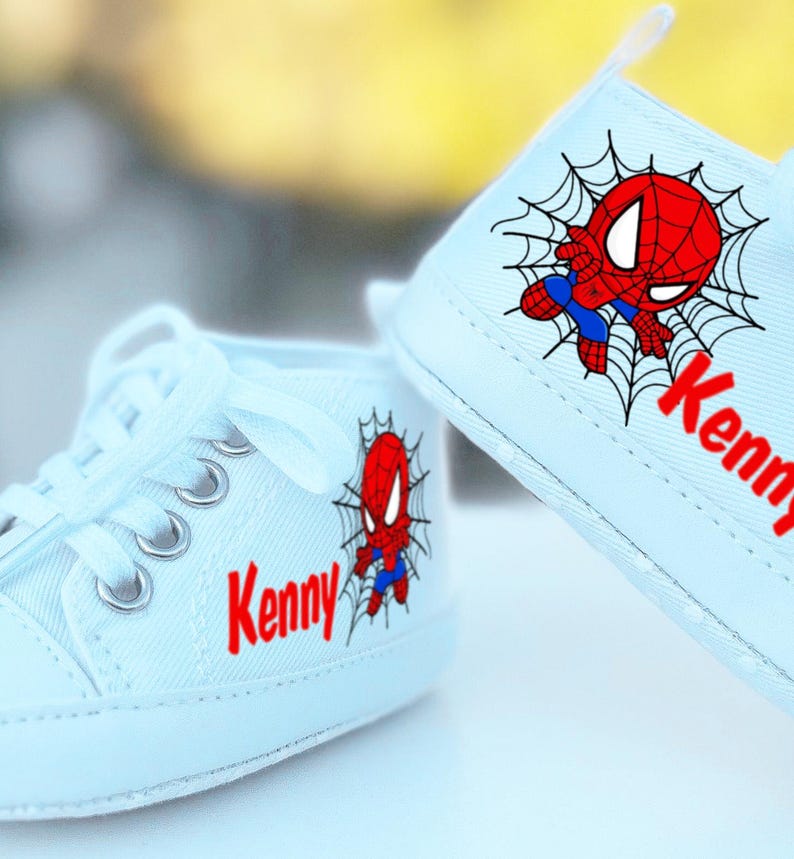 May include: A pair of light blue baby shoes with a Spiderman design and the name "Kenny" on each shoe.