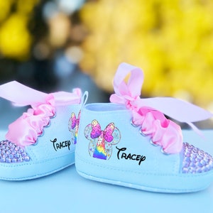 May include: A pair of light blue baby shoes with pink satin bows and rhinestones. The shoes have a rainbow and Mickey Mouse design with the name "Tracey" written on them.