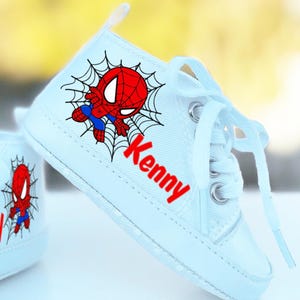 May include: White canvas baby shoes with a red and blue Spiderman design and the name "Kenny" written in red letters.