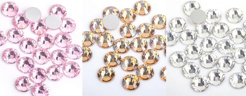May include: A collection of round, faceted rhinestones in three colors: light pink, golden amber, and clear crystal. Each rhinestone has a flat, silver backing. The gems are scattered, showcasing their sparkle and clarity, ideal for craft projects.