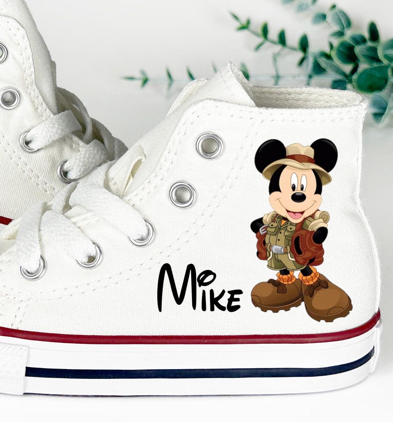 May include: White high-top canvas sneakers with red and blue trim. Features a cartoon graphic of Mickey Mouse in safari attire. The name "Mike" is printed in black script on the side.