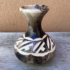 May include: A decorative vase with a bulbous body and a narrow neck. The vase is primarily black and gray, with a white geometric pattern around the middle. The rim has a light gray color.